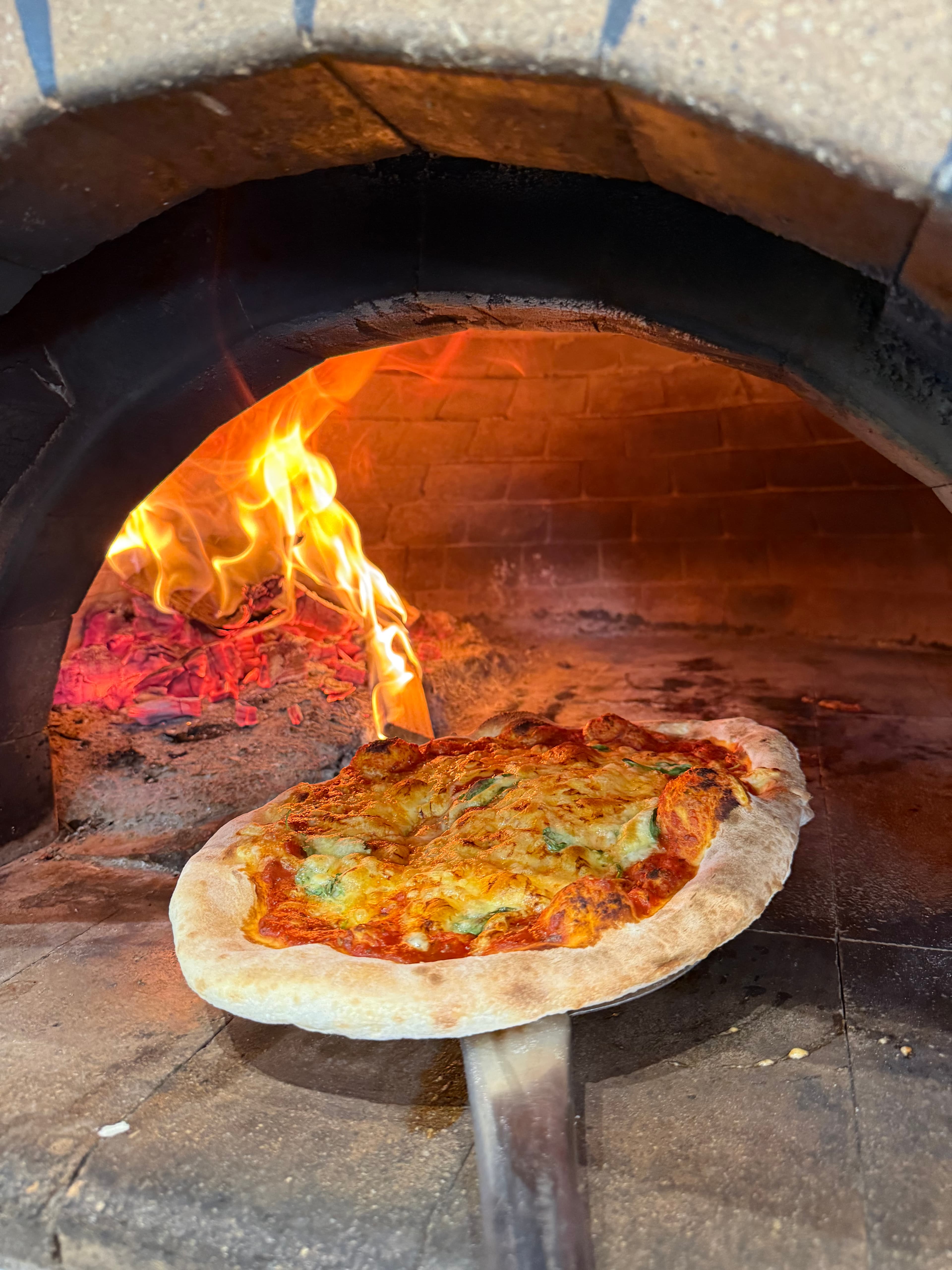 Fresh pizza with melted cheese and tomato sauce cooking inside a roaring wood-fired brick oven.